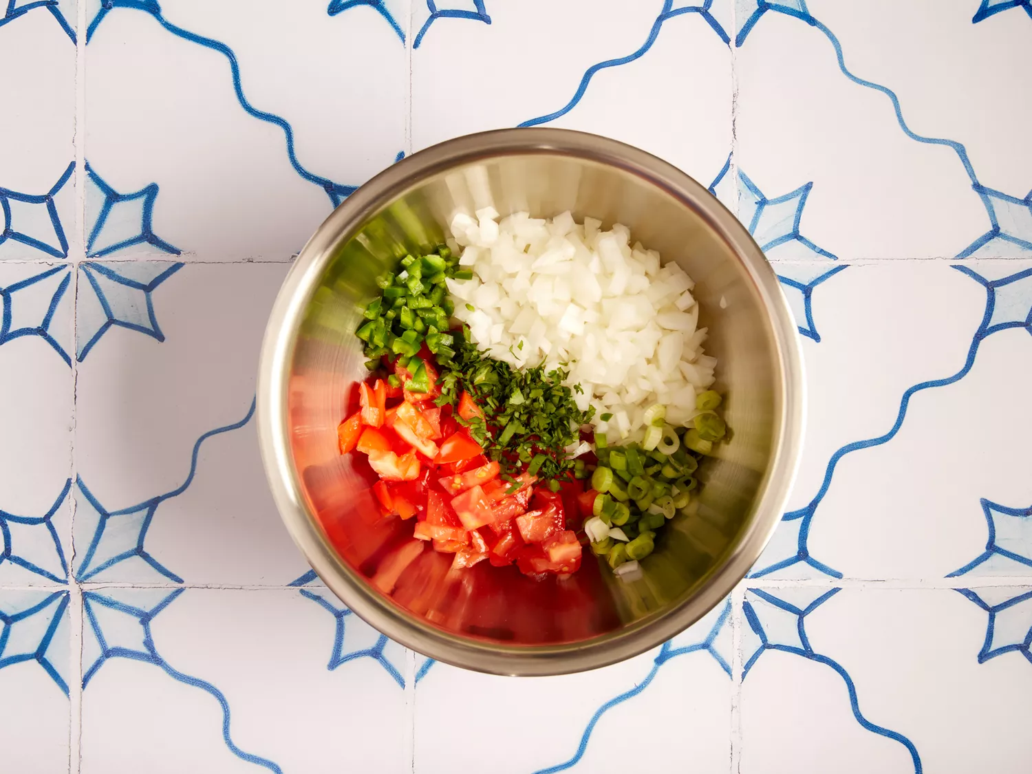 Diced tomatoes, onions, and peppers in a metal bowl. 