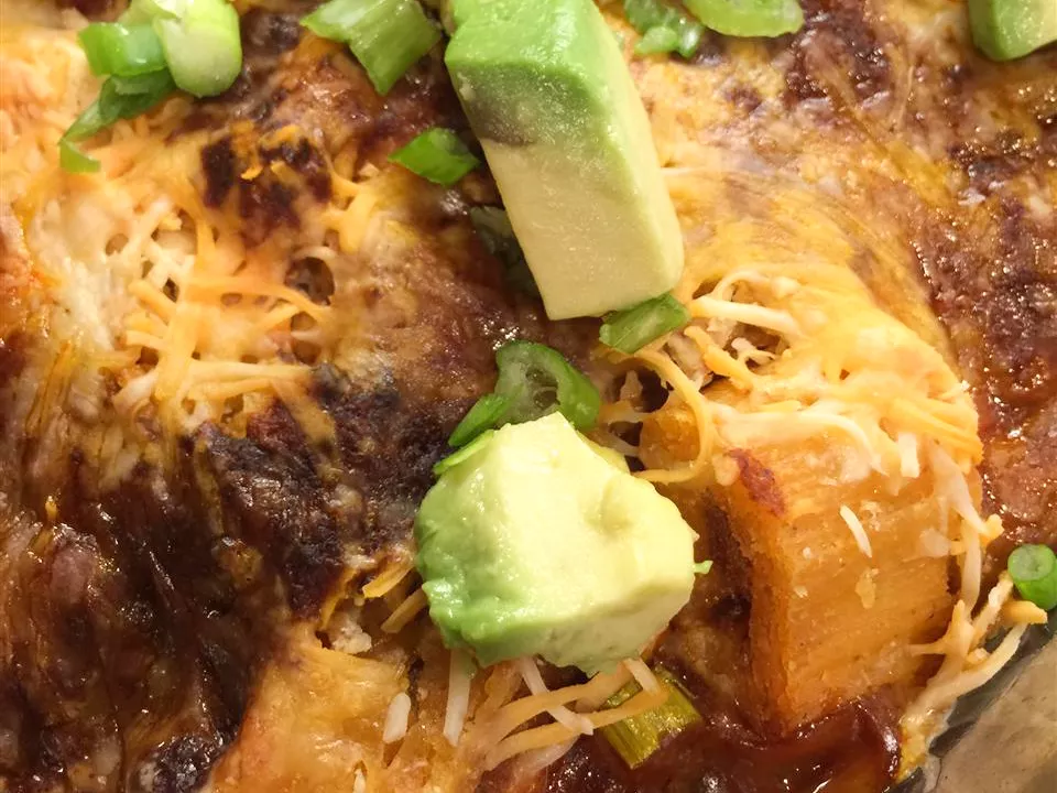 Close up view of a tamale casserole with cheese and avocados on top in a glass baking dish