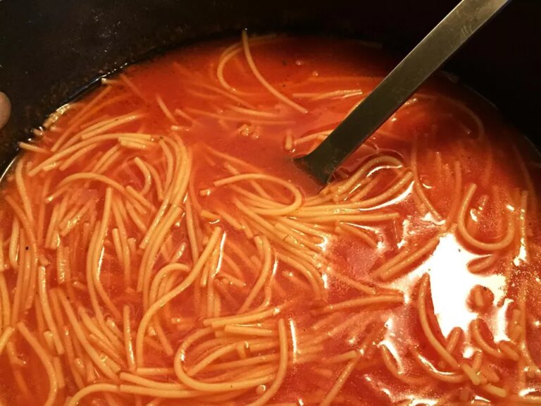 Close up view of sopa de fideos in a black pot with a ladle