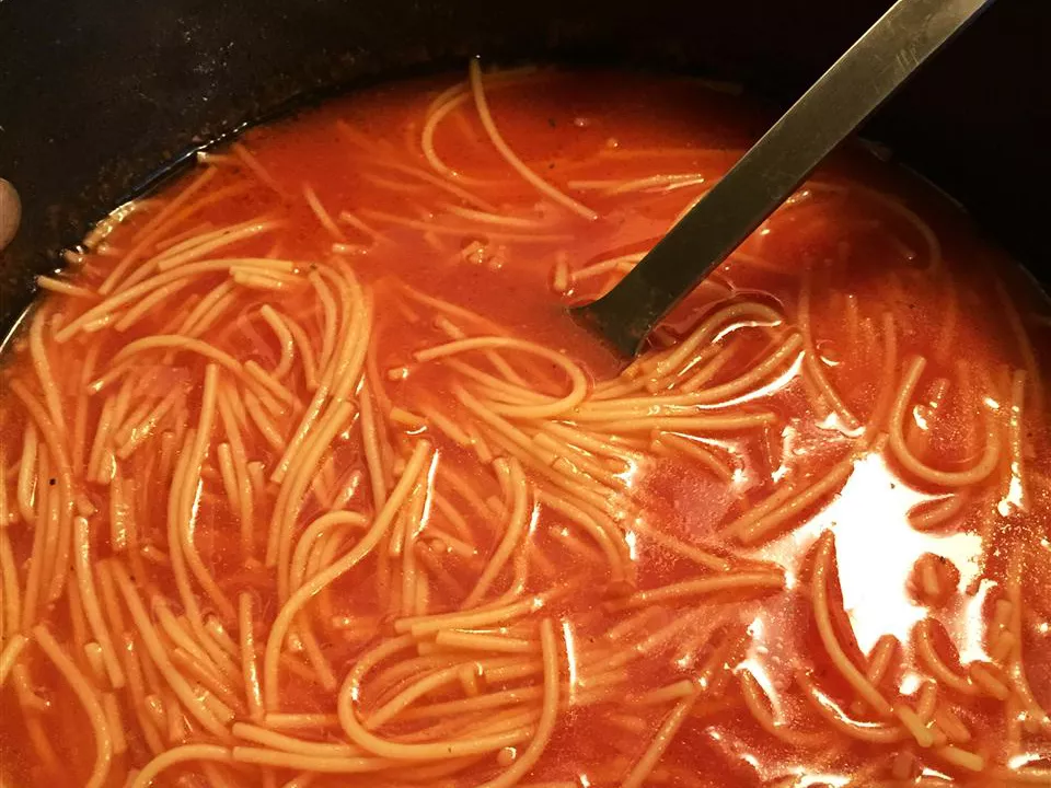 Close up view of sopa de fideos in a black pot with a ladle