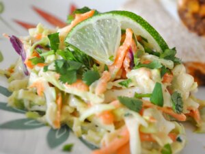 Close up view of texas coleslaw with cabbage, carrots and herbs, garnished with a lime slice on a plate