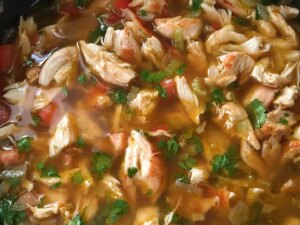 Close up view of mexican chicken soup with fresh herbs in a pot