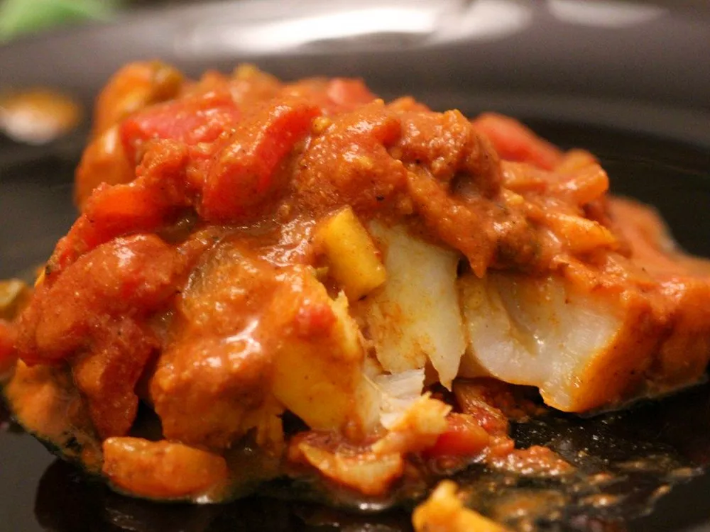Close up view of cod curry on a black plate