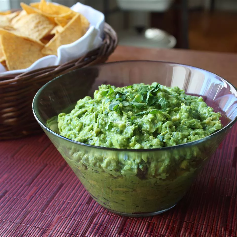 Close up view of classic guacamole in a glass bowl, served with tortilla chips in a basket