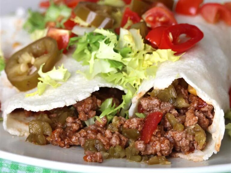 Close up view of spicy beef burritos garnished with lettuce, tomatoes and pickled jalapeños on a plate