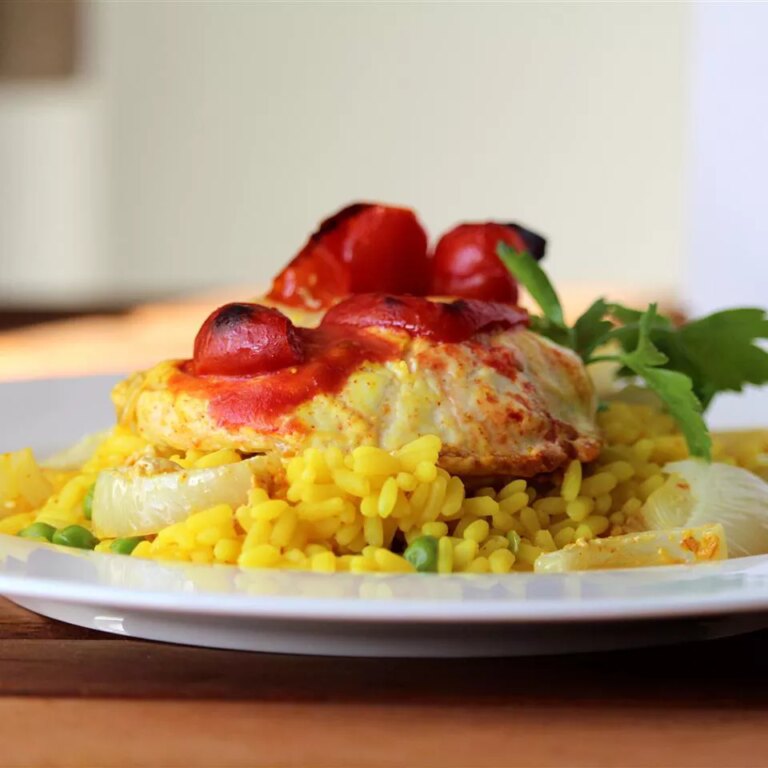 Close up view of biryani with yogurt marinated chicken garnished with fresh herbs on a white plate