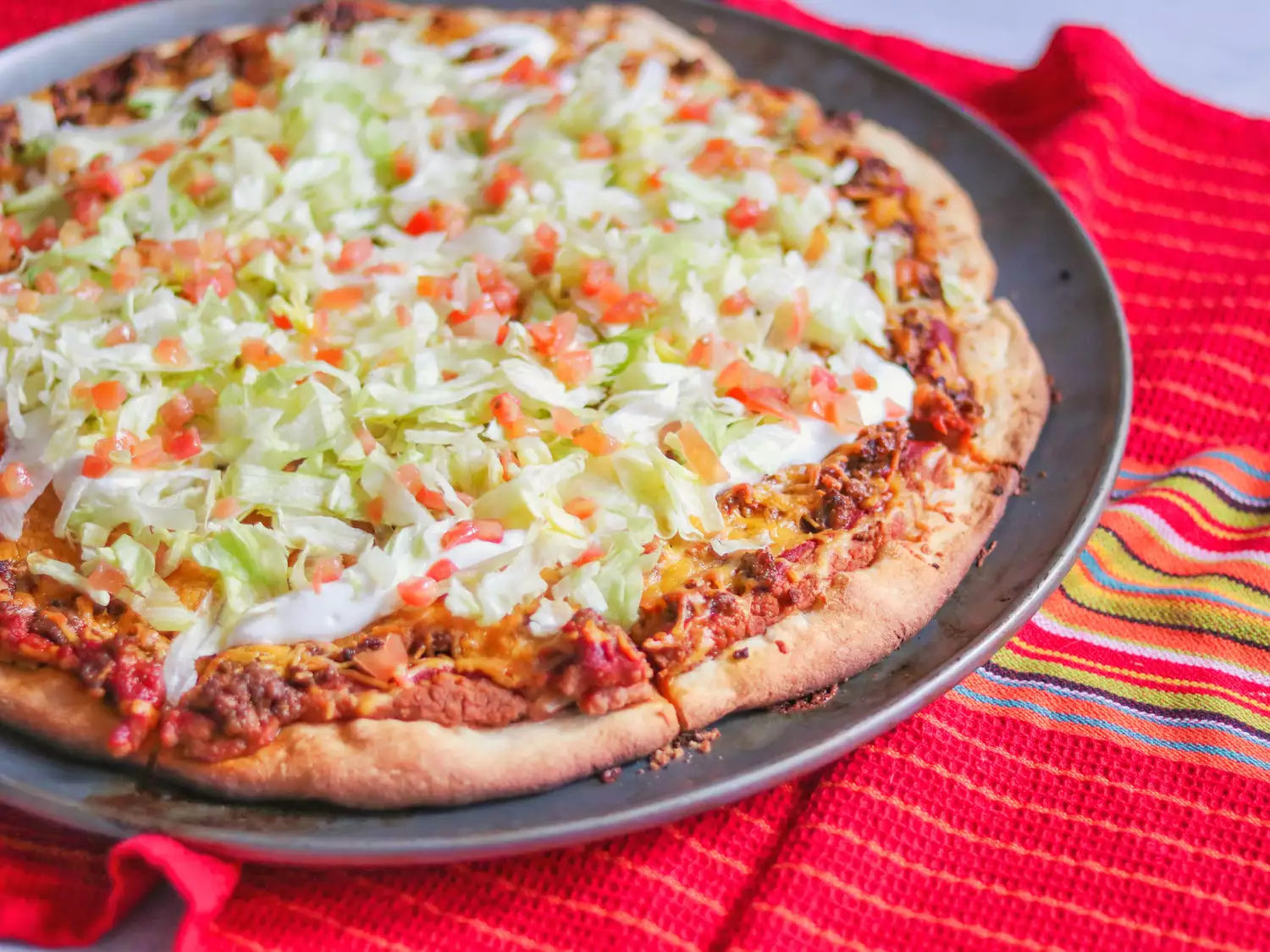 Taco pizza topped with lettuce and tomatoes