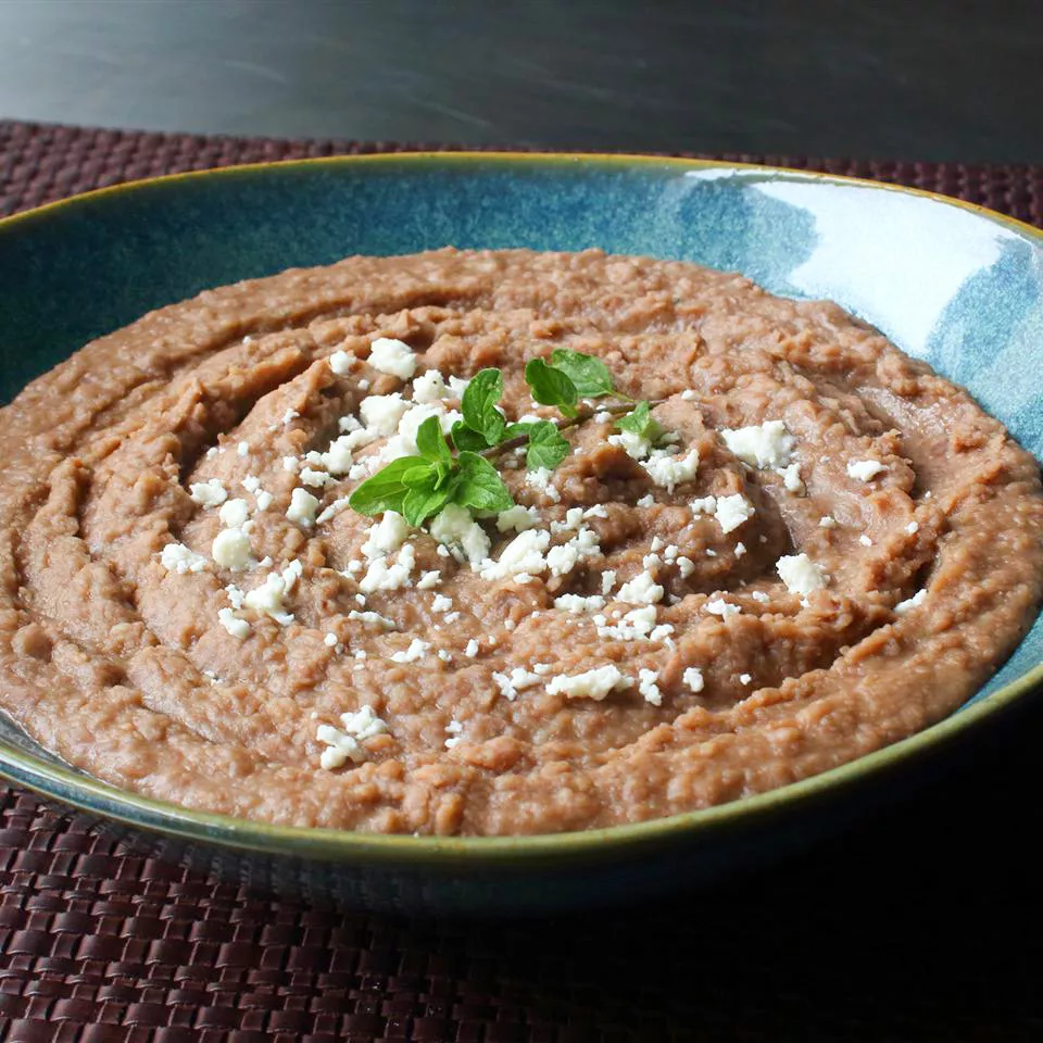Close up view of refried beans in a bowl, garnished with cheese and fresh herbs