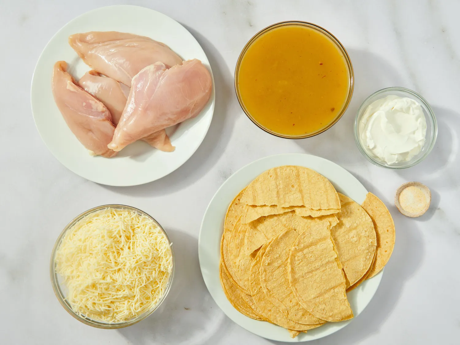 Ingredients for a green chile chicken enchilada casserole including raw chicken shredded cheese tortillas green chile sauce and seasoning