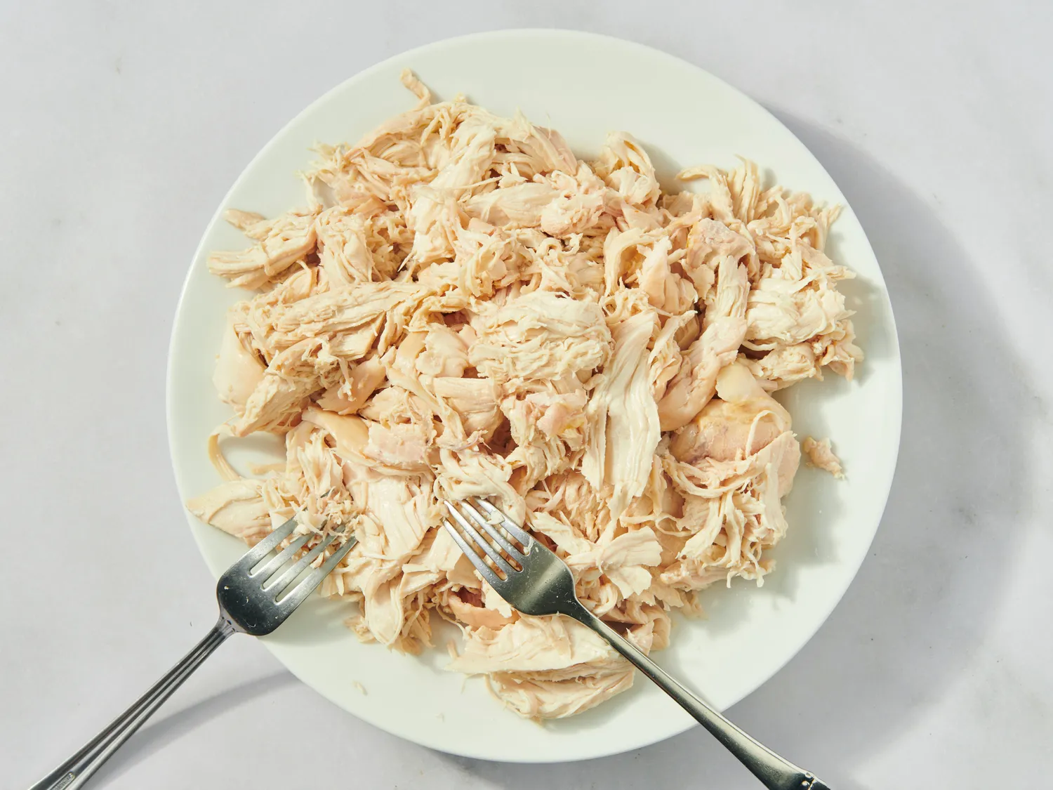 Shredded chicken on a white plate with two forks