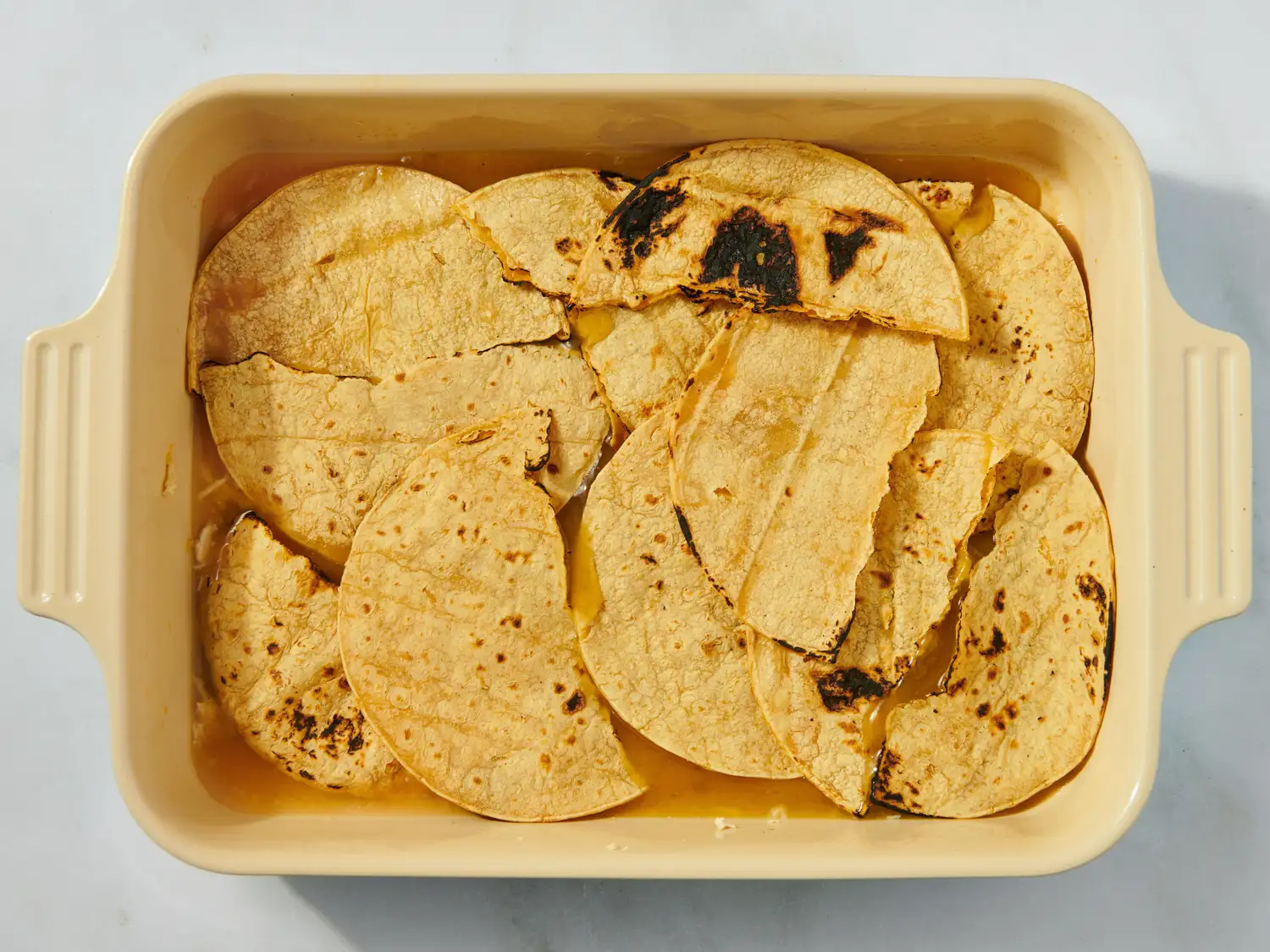 Baking dish with layered toasted tortilla pieces part of an enchilada casserole preparation