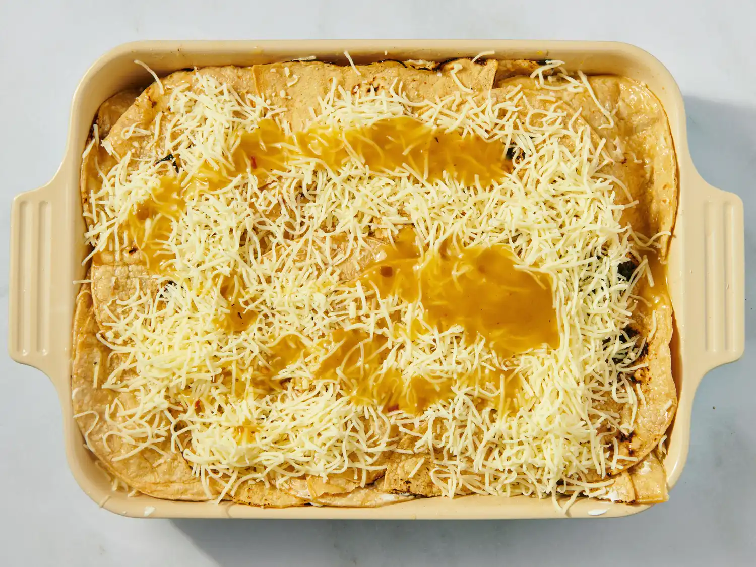 A casserole dish with green chile chicken enchiladas topped with cheese and green sauce