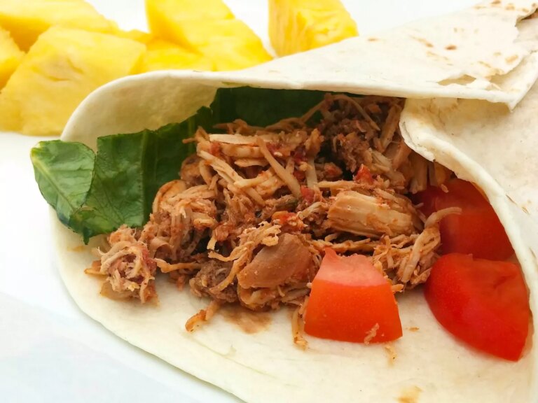 Close up view of slow cooker chicken tinga with a tortilla, lettuce and tomato, served with pineapple on a plate