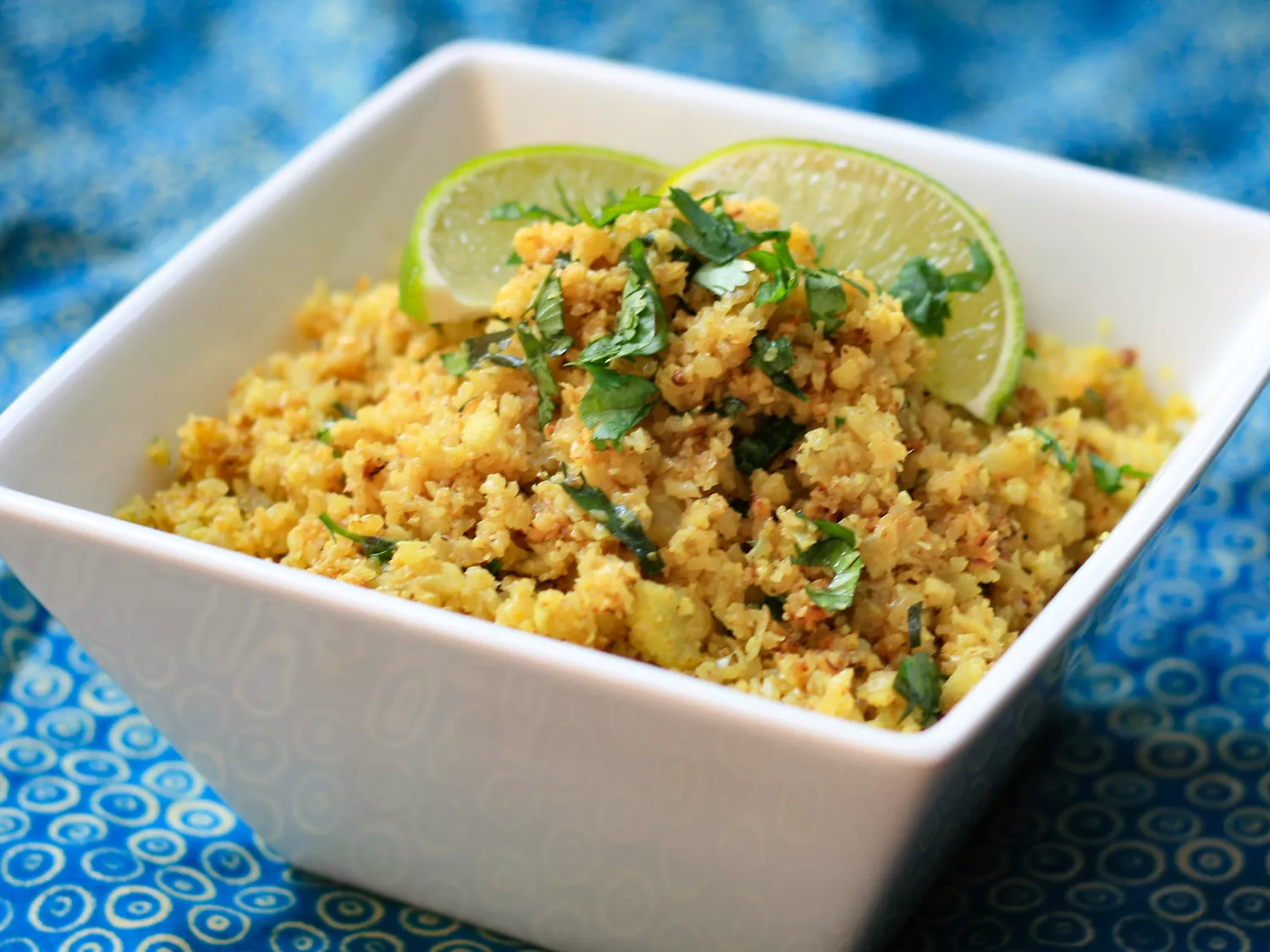 Close up view of cauliflower rice (biryani style) garnished with fresh herbs and lime wedges in a white bowl