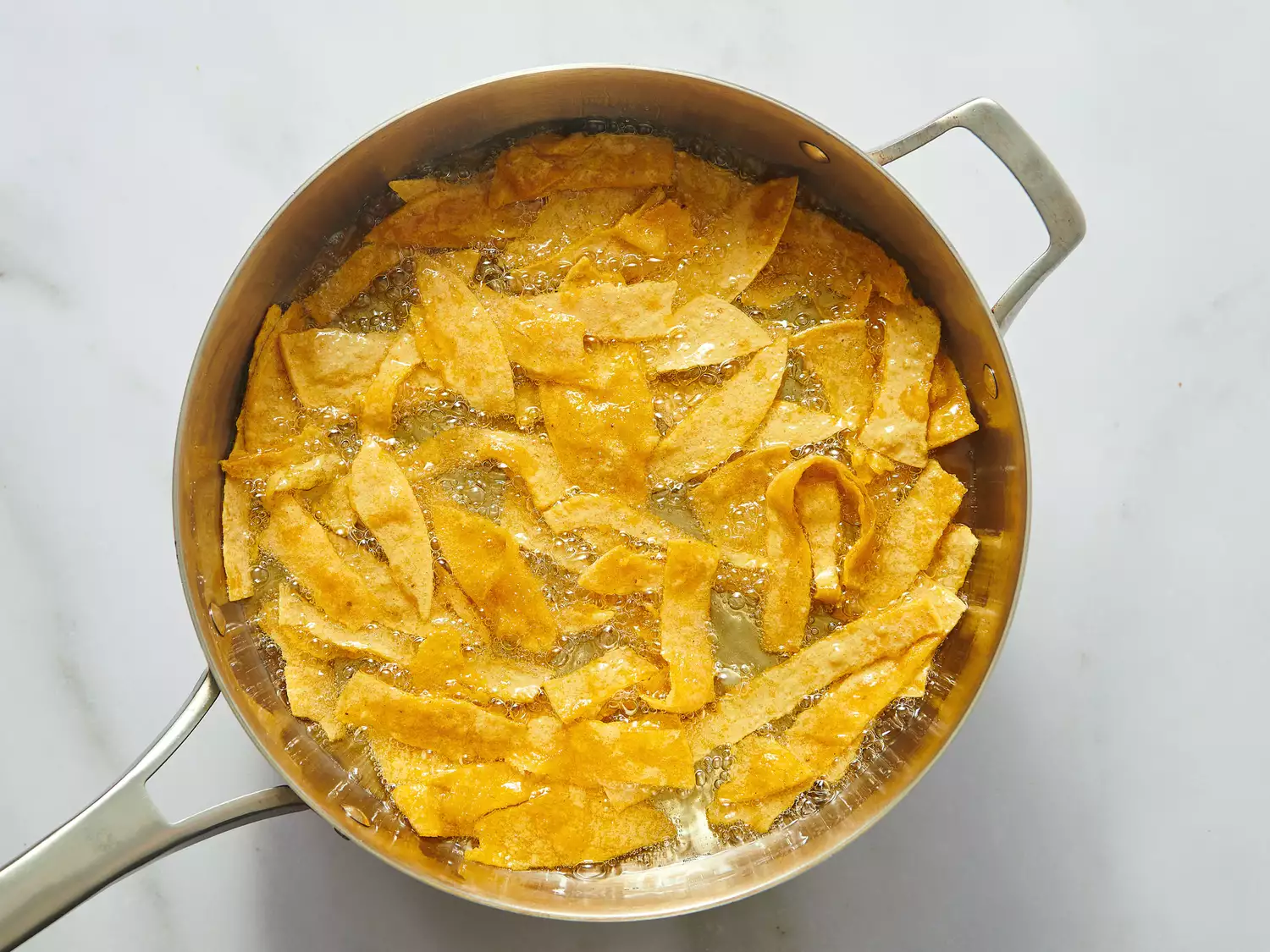 Tortilla chips frying in a pan filled with oil, part of a cooking process