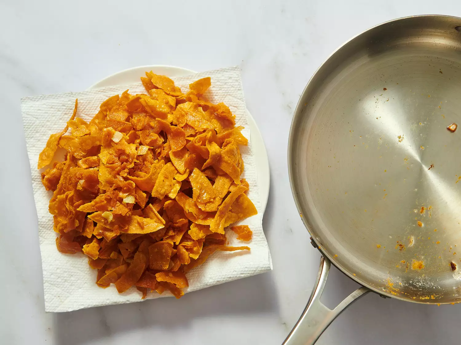 Fried tortilla pieces on a paper towel next to a pan