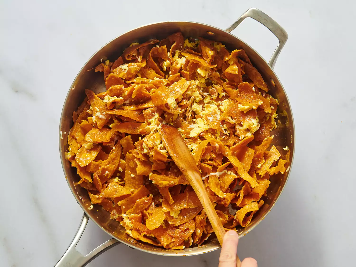 A pan of cooked chilaquiles being stirred with a wooden spoon