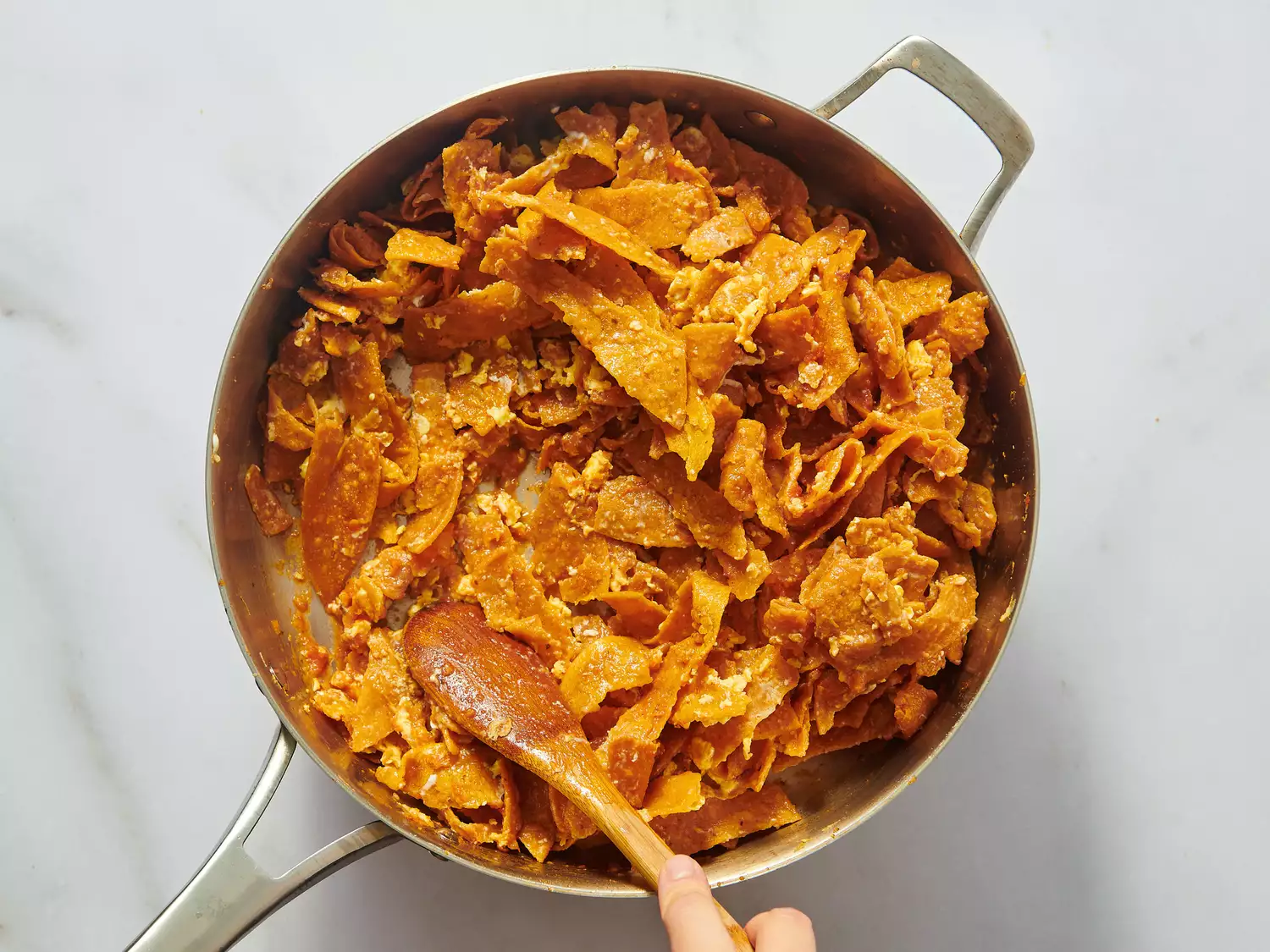 Cooking chilaquiles in a pan with a wooden spoon being used to stir