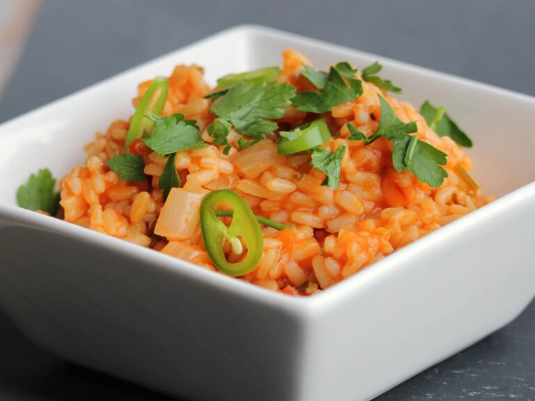 Close up view of spanish rice garnished with fresh herbs and jalapeños in a white bowl