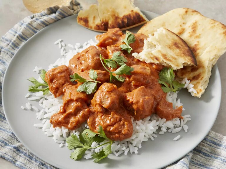 High angle looking at a plate of chicken makhani over rice, topped with cilantro and a side of naan bread
