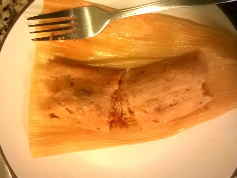 Close up view of a red chicken tamale (tamale rojos de pollo) on a plate with a fork