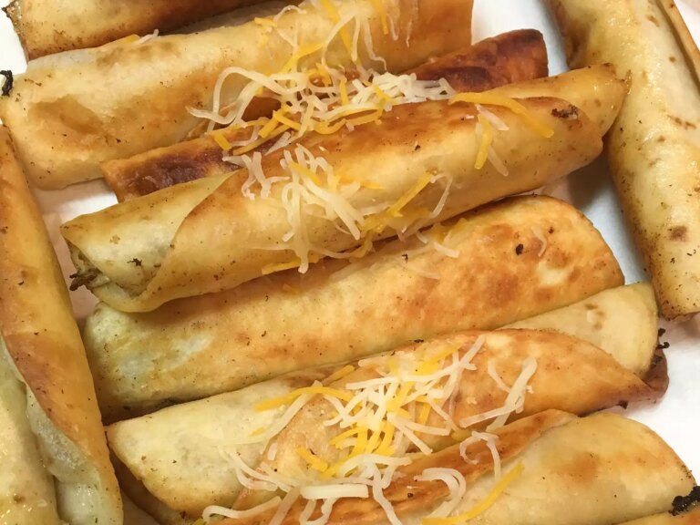 Close up view of chicken taquitos with cheese on a white platter