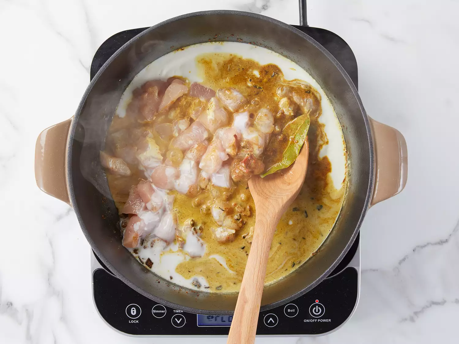 Raw chicken, coconut milk, and other spices cooking in a skillet. 