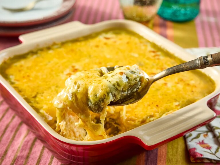 Casserole dish containing chili rellenos with a spoon lifting a serving from the dish