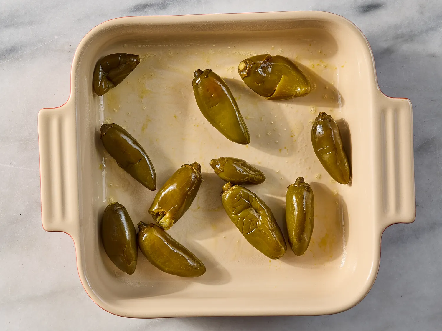 A baking dish containing roasted green chili peppers part of a recipe preparation step