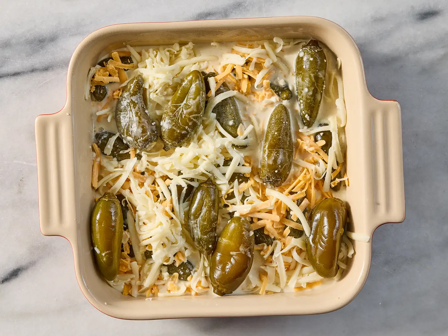A baking dish with layers of cheese and whole green chili peppers prepared for baking