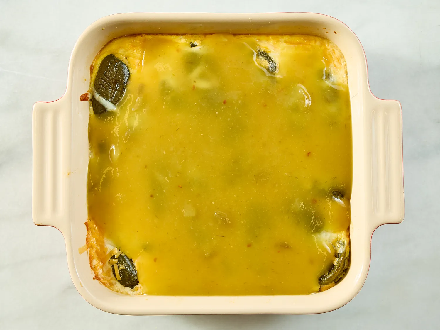 Casserole dish with cooked chile relleno mixture topped with a yellow sauce