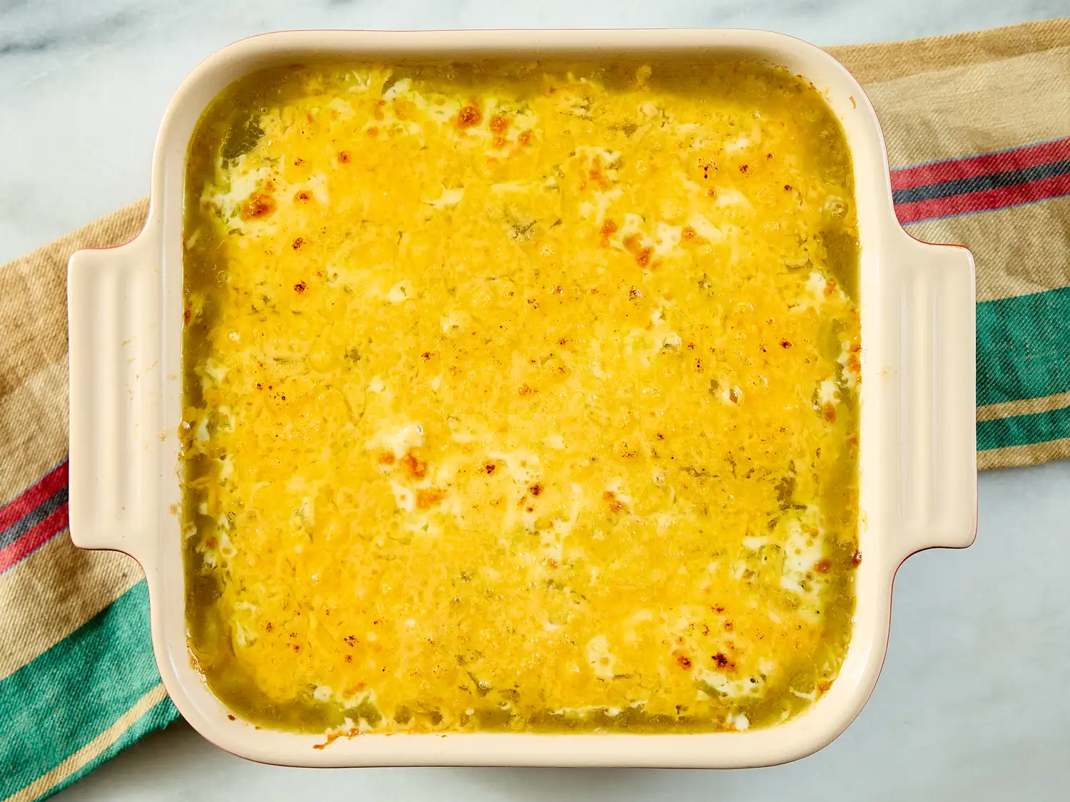 A casserole dish with baked chili rellenos casserole placed on a decorative cloth