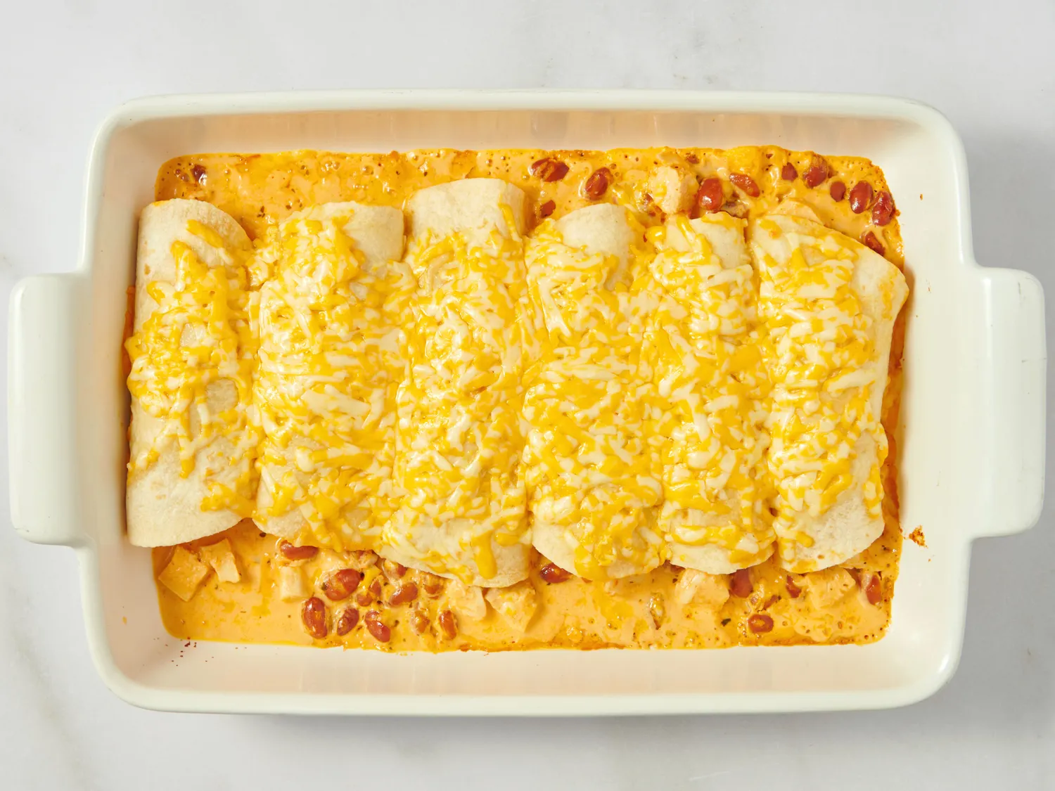 A baking dish containing six chicken enchiladas covered with melted cheese