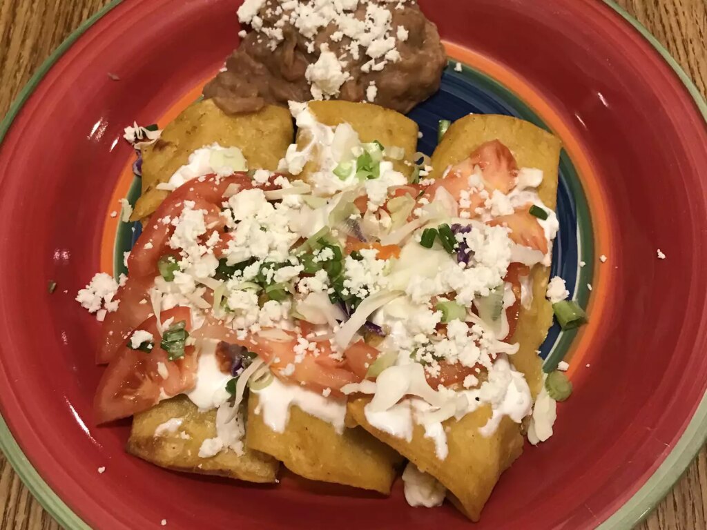 Close up view of authentic mexican enchiladas garnished with cheese, served with refried beans on a colorful plate