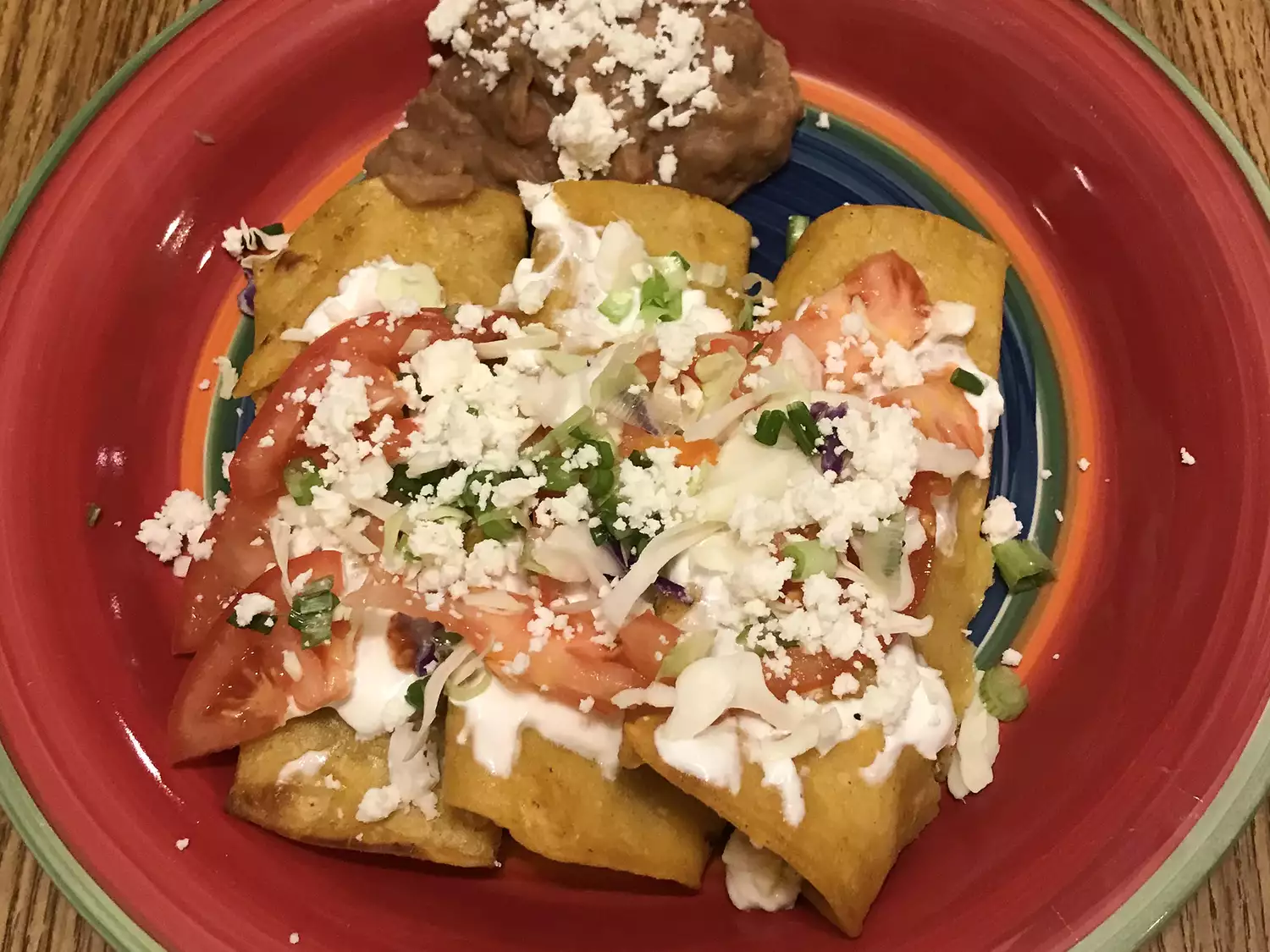 Close up view of authentic mexican enchiladas garnished with cheese, served with refried beans on a colorful plate