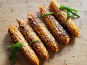 5 ears of mexican grilled corn topped with grated cotija and garnished with green onions on a wooden cutting board