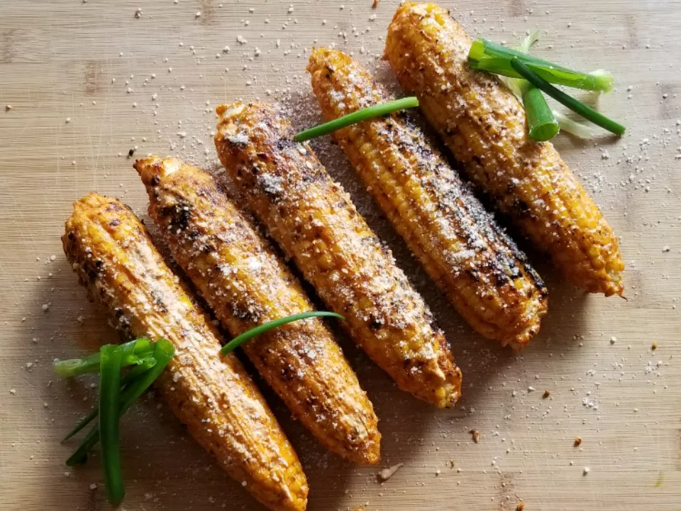 5 ears of mexican grilled corn topped with grated cotija and garnished with green onions on a wooden cutting board