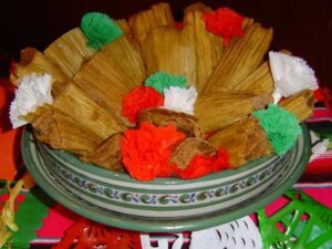 Close up view of tamales de frijoles (bean tamales) garnished with green, red and white paper flower, in a green bowl