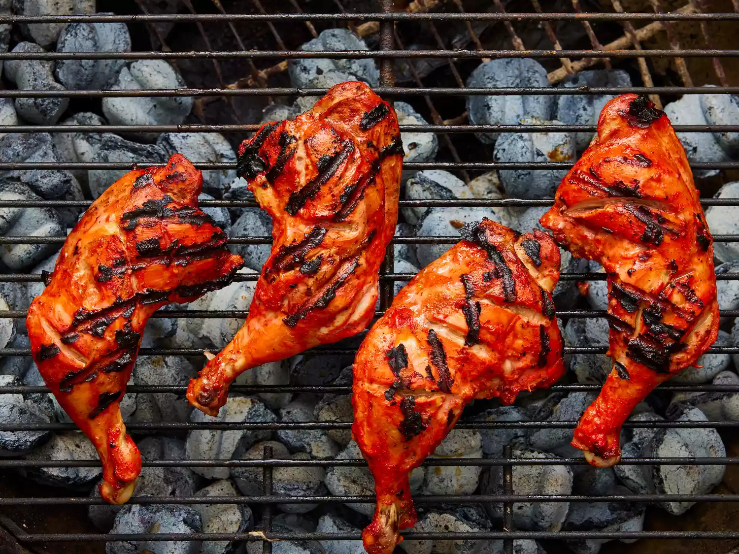 an overhead view of tandoori style bone in chicken being cooked on a hot grill. 