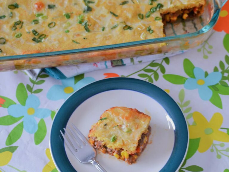 Close up view of a slice of mexican corn bread casserole and mexican corn bread casserole in a glass baking dish