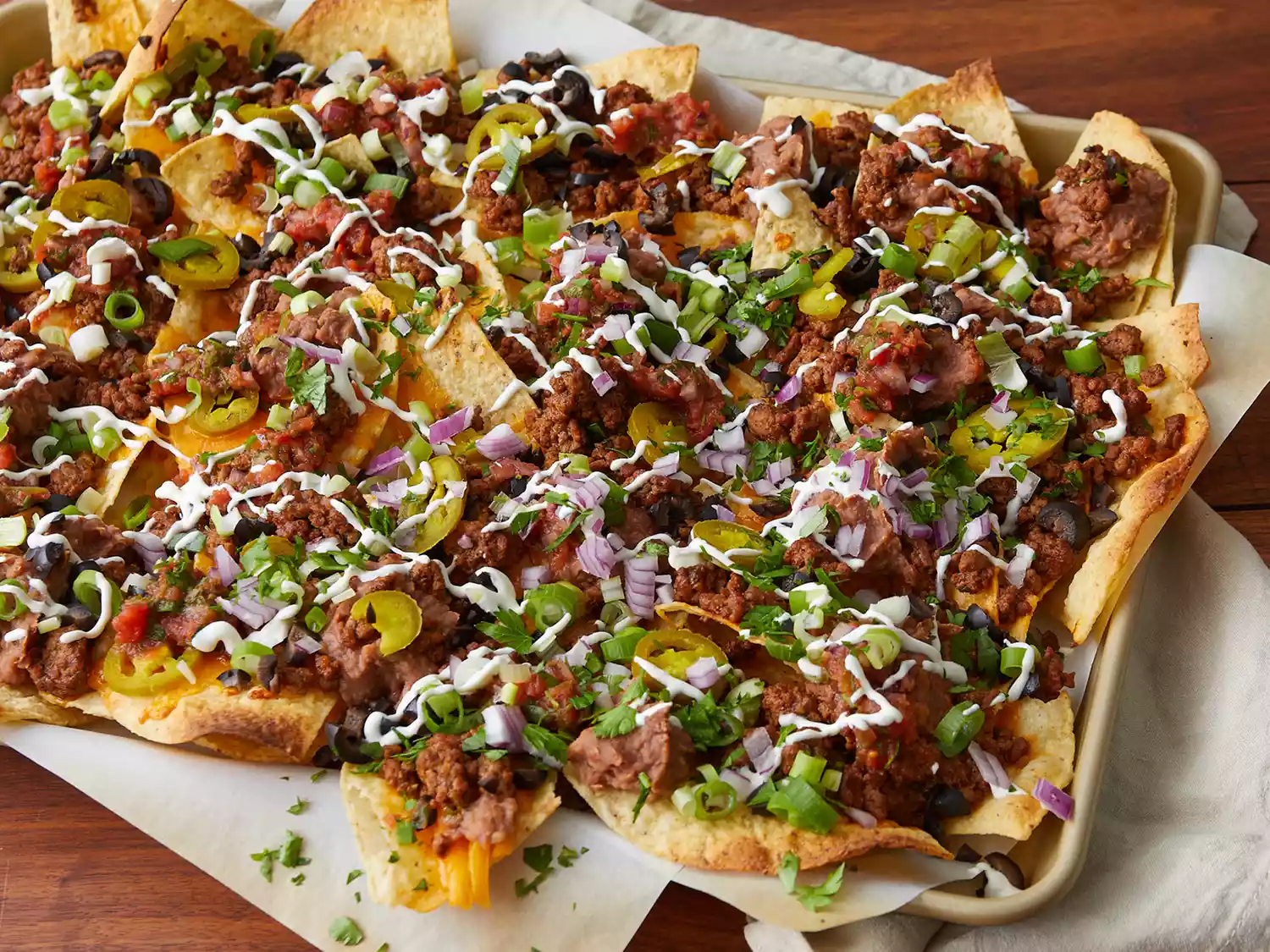 close up on a baking sheet of super nachos garnished with green onions and jalapeños 