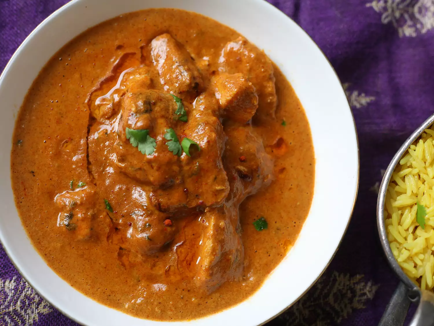 Close up view of indian chicken tikka masala garnished with fresh herbs in a white bowl, served with rice