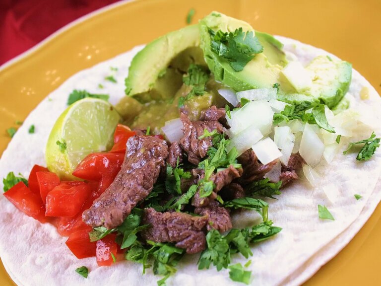 Close up view of a carne asada taco garnished with fresh herbs on a yellow plate