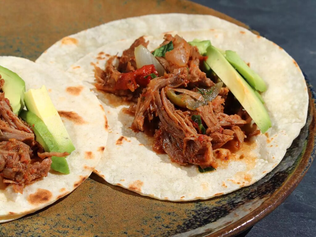 Close up view of shredded beef tacos with avocado pieces on a plate
