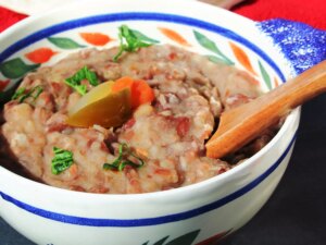 Close up view of vegetarian refried beans garnished with peppers, carrots and fresh herbs in a bowl with a wooden spoon