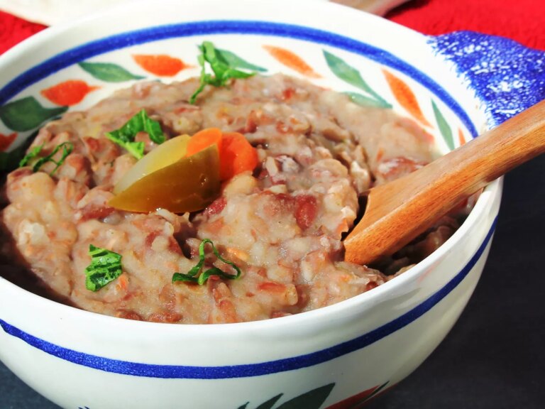 Close up view of vegetarian refried beans garnished with peppers, carrots and fresh herbs in a bowl with a wooden spoon