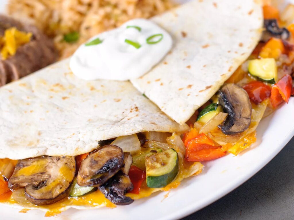 Close up view of a vegetarian quesadillas garnished with sour cream and green onions, with rice in the background