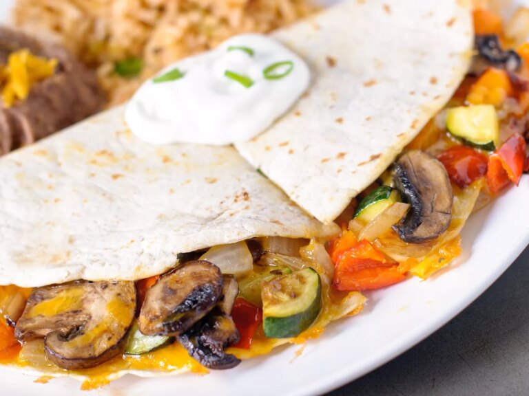 Close up view of a vegetarian quesadillas garnished with sour cream and green onions, with rice in the background