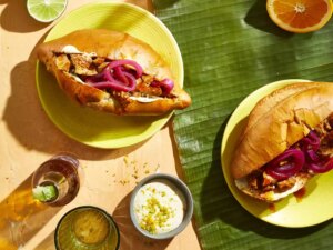2 mexican sandwiches with pulled pork inside rolls topped with pickled red onions on yellow plates