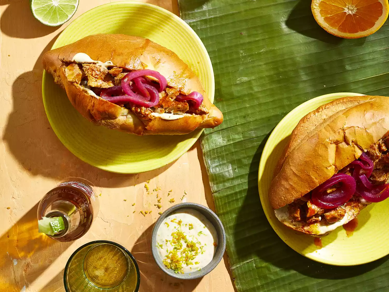 2 mexican sandwiches with pulled pork inside rolls topped with pickled red onions on yellow plates